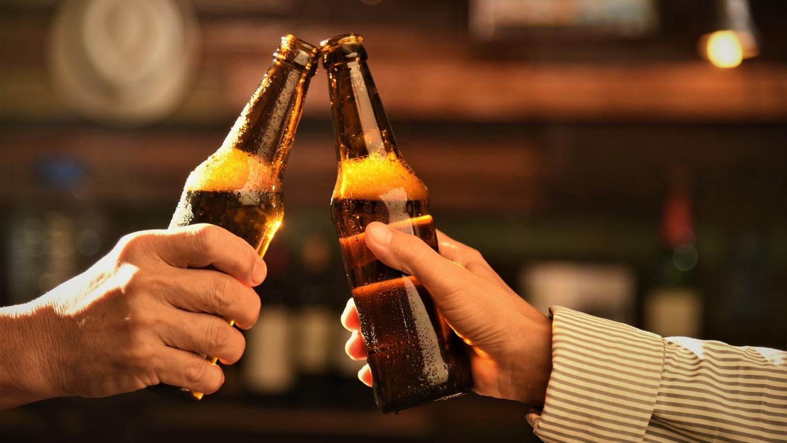 two male hands hold glass brown bottles of beer