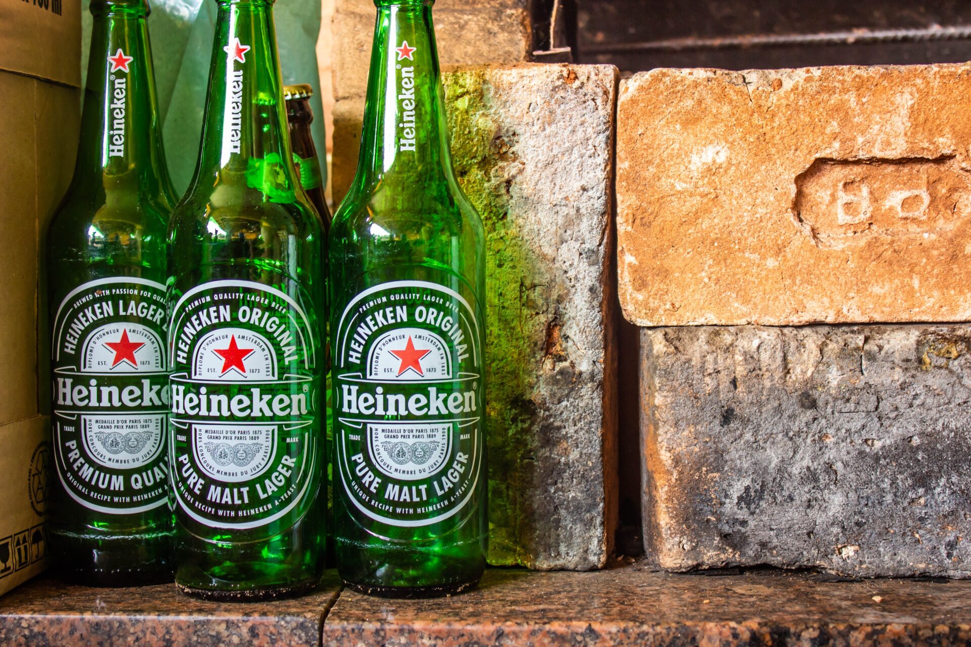 3 green bottles of Heineken beer near brown bricks