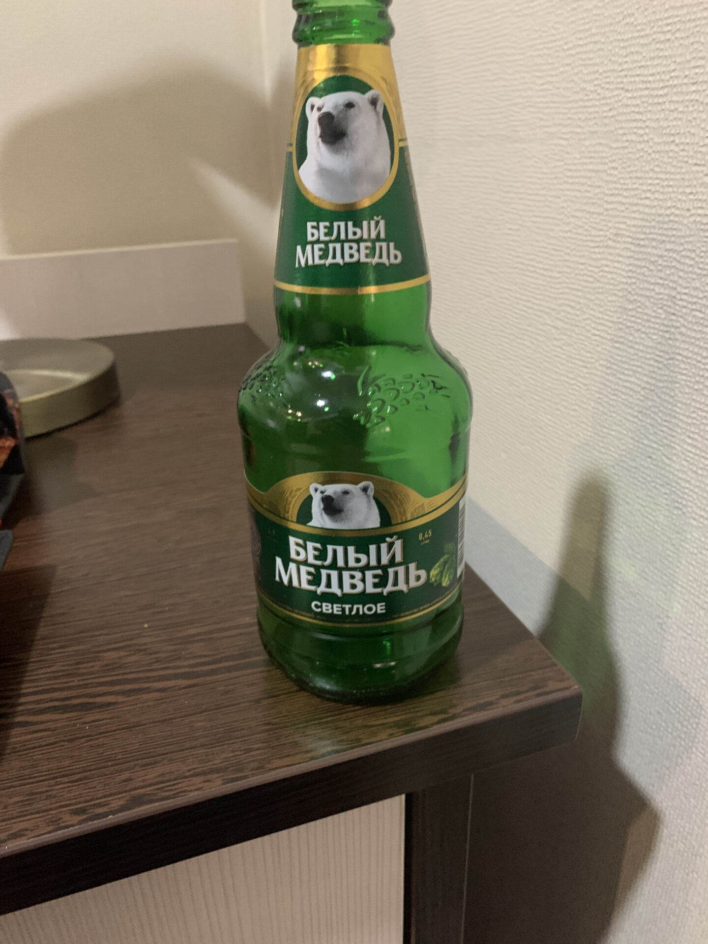 Ukrainian light beer "Bilyi Medved" (White Bear) is standing on a table next to the wall. The bottle is 0.5 liters and is green in color.