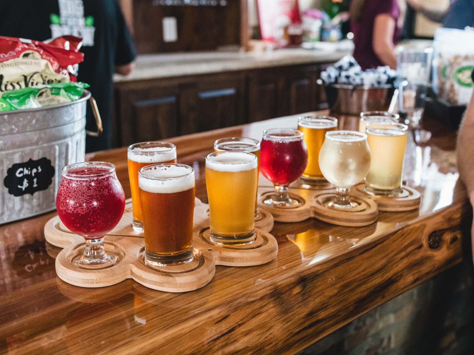 many glasses of different shapes with different types of beer on a wooden bar counter in a bar